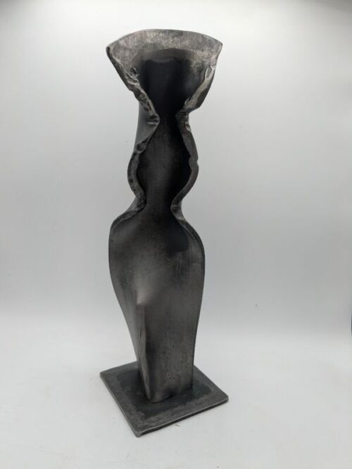 Metal Table Sculpture - Forged Flow - Modern Abstract Art One of a kind - original art by Nathaniel Winkler   Dimensions: 13"X4"X4" This hand-forged steel sculpture explores the tension between strength and softness. Though born from rigid metal, the form carries the fluidity of fabric, its folds and curves capturing a moment of movement frozen in time. The darkened, textured surface reveals the raw beauty of the forging process, where heat and hammering coax steel into unexpected elegance. Standing tall on a solid base, the piece invites viewers to see strength not as something fixed and unyielding, but as something capable of bending, flowing, and transforming. Its abstract form evokes both the human figure and natural forces, leaving space for individual interpretation and emotional connection. Each angle reveals a new perspective—harsh edges soften into curves, shadows deepen, and the material’s industrial origins dissolve into organic grace.